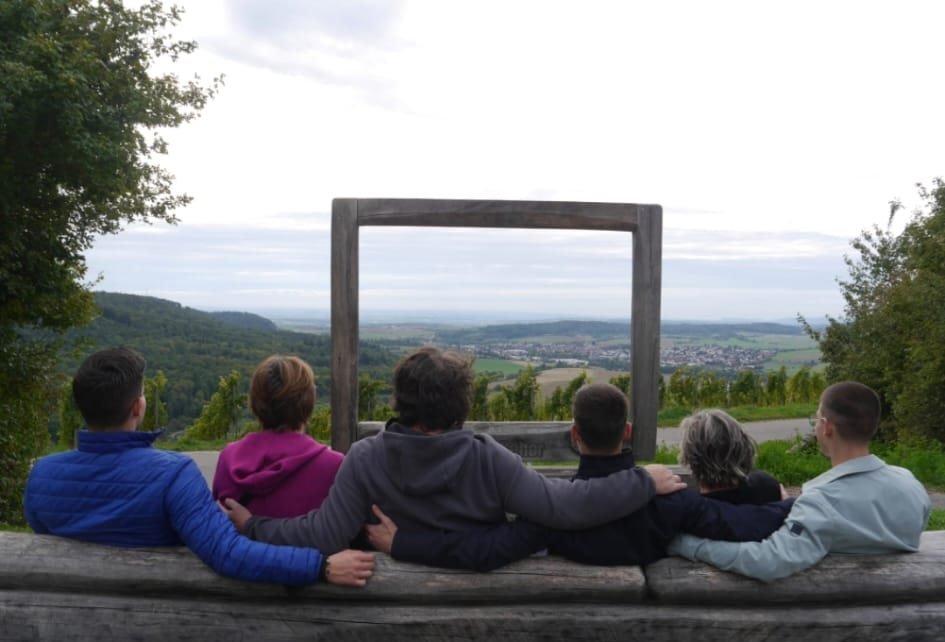 The family sitting with their backs to the camera on a wooden bench in front of a large wooden frame at Burg Lichtenberg